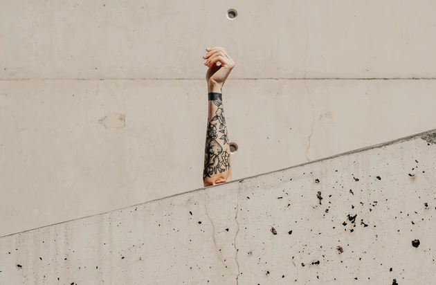 コンクリートのスキマから、まっすぐにのばされたタトゥーの入った女性の左手