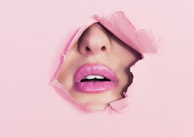 ピンクの穴からのぞくピンクの口紅をした女性の顔の見える風景