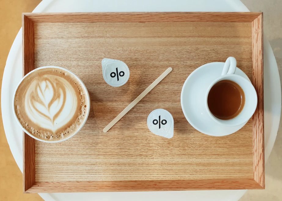 カフェラテとコーヒーと、ミルクとマドラーで％の文字を象った文字をトレイに乗せた風景