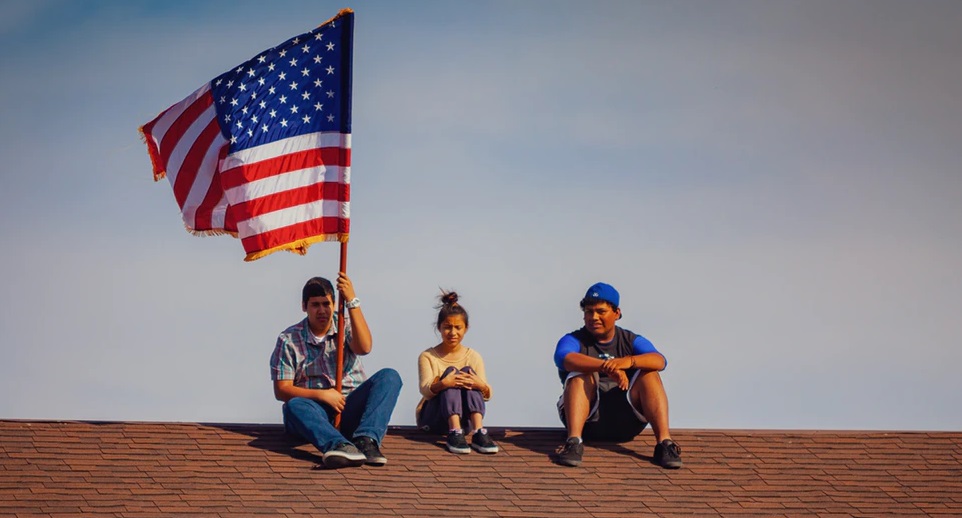 屋根上に上り、アメリカ国旗を掲げる3人の子供のいる風景